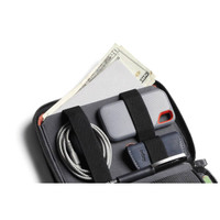 A grey toiletry bag with compartments holding cash, a phone case, a cable, and a pen against a dark background.