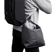 A cooler bag in a grid pattern, featuring a shoulder strap, being carried on the side of a person with a backpack.