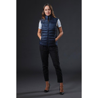 A navy women's puffer vest is displayed on a model, featuring a sleek design and a logo. The model wears black pants and heels.