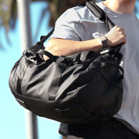 A black duffel bag with sturdy straps and textured detailing, being held by a person.