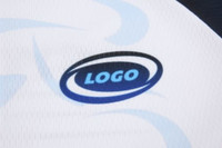 A close-up of a white sports jersey featuring a logo in blue and black. The fabric has a textured pattern.