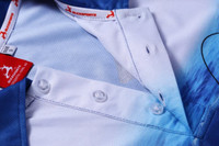 A close-up of a blue and white fishing polo with buttons and a tag, featuring a logo.