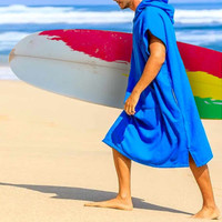 A blue cotton surf poncho with a hood, worn by a person carrying a surfboard on the beach.