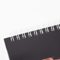 A black desk calendar with a spiral binding at the top, featuring a smooth, matte cover.