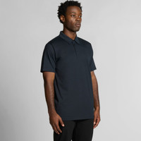 A black polo shirt on a model, featuring a collar and short sleeves, with a logo on the chest.