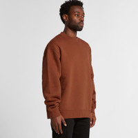 A man wearing a brown sweater stands sideways, showcasing the relaxed fit and style of the garment.