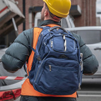 A navy blue backpack with multiple compartments and a logo, worn by a person in an orange vest and hard hat.