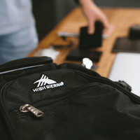 A black High Sierra Access 3.0 Backpack with a logo, resting on a table among various items.