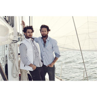 Two men posing on a sailboat, one wearing a light blue button-up shirt and the other in a white vest over a checked shirt.