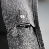 A close-up of a grey fabric backpack strap featuring a USB port and subtle branding.