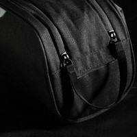 A black toiletry bag with straps and zippers, featuring a textured fabric and branding.
