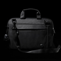 A black laptop sleeve with a handle and adjustable strap, featuring a front pocket and a small attached keychain.