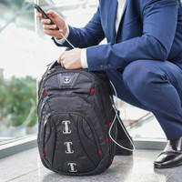 A black Swissdigital Pixel Backpack with red accents, positioned on the floor near a person using a phone.