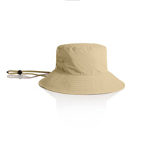 A beige nylon wide brim bucket hat with a corded chin strap and an attached logo.