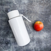 A drink bottle in white with a straw, positioned next to a red apple on a textured grey surface.