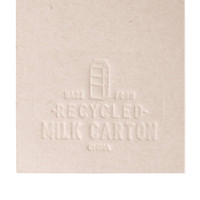 A beige bookmark shaped like a milk carton, made from recycled materials, featuring an embossed design and a logo.
