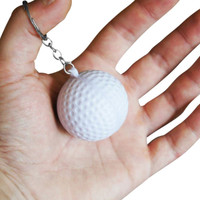 A white golf ball stress reliever attached to a silver keyring, held in a person's hand.