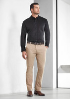 A man wearing a black long sleeve shirt paired with beige trousers and brown shoes, standing against a plain background.