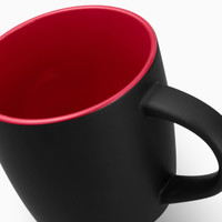 A coffee mug with a matte black exterior and a red interior, featuring a handle and a logo.
