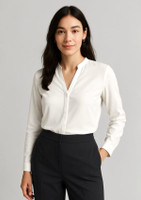 A white long sleeve blouse with a collar, worn by a woman, paired with dark trousers. Branding is present.
