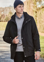 A model wearing a black jacket and a navy beanie, standing outdoors with greenery in the background.