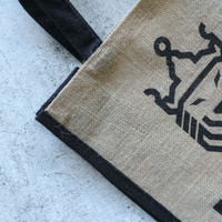 A jute tote bag featuring a natural brown body with a black trim and logo.
