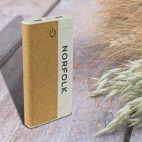 A wireless eco power bank in natural tones, featuring a logo and two USB ports on a wooden surface with grass.