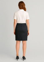 A woman in a white polo shirt and dark mid waist stretch chino skirt, facing away from the camera.