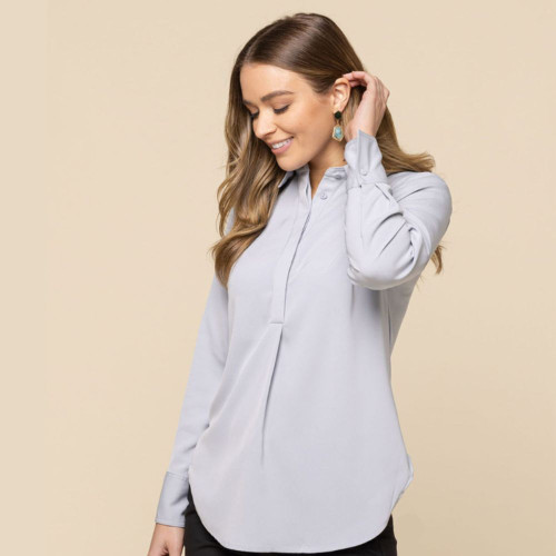 Woman wearing a stylish light grey blouse, posing with a gentle smile against a neutral background.