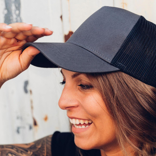 A grey trucker cap with a mesh back, being worn by a person smiling. A grey trucker cap with a mesh back, being worn by a person smiling.