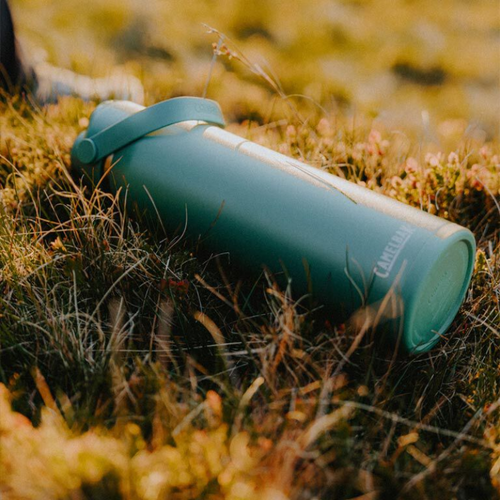 Green Camelbak thrive water bottle lying in grass