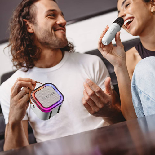 A portable karaoke machine in black with colourful lights, being used with a microphone by two people.