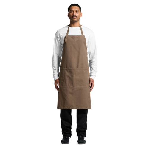 A brown canvas apron worn by a model, featuring a front pocket and adjustable neck straps.