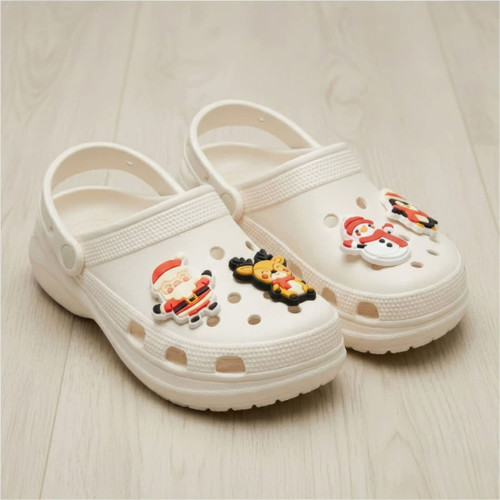 A pair of white clogs featuring festive shoe charms, including Santa and a snowman.