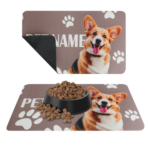 A pet feeding mat featuring a brown background with a corgi's face and paw print designs. It has a logo.
