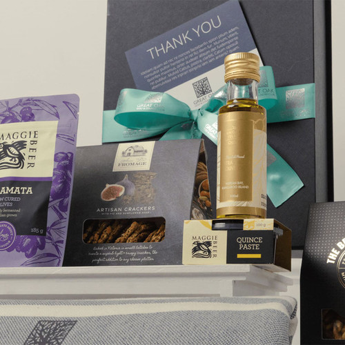 A gourmet gift pack featuring a bottle of quince paste, artisan crackers, and assorted treats in purple and black packaging.