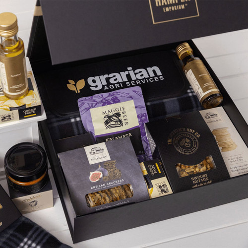 A gourmet picnic gift pack filled with olive oil, crackers, nuts, honey, and a branded box in black and white.