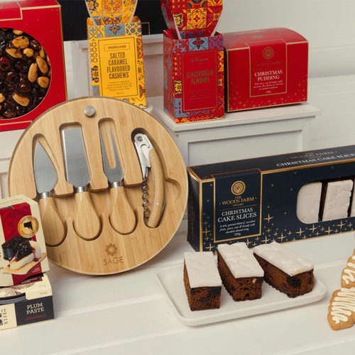 A bamboo serving board with knives, a corkscrew, and assorted festive snacks in red and gold packaging.