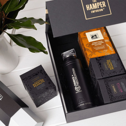 A drink bottle and assorted snack boxes, including roasted peanuts, in a black gift pack with a logo.