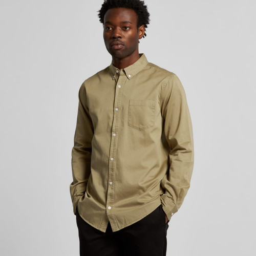 A button-up denim wash shirt in olive green, featuring a chest pocket and a collared neck, modelled by a young man. A button-up denim wash shirt in olive green, featuring a chest pocket and a collared neck, modelled by a young man.