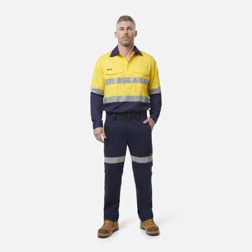 A man wearing KingGee navy blue work pants with reflective tape and a yellow and blue work shirt
