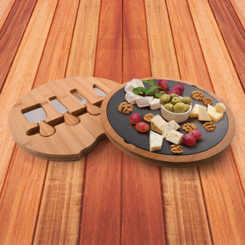 A bamboo cheese board with a slate surface, featuring assorted cheeses, olives, grapes, and walnuts. It includes knife slots.