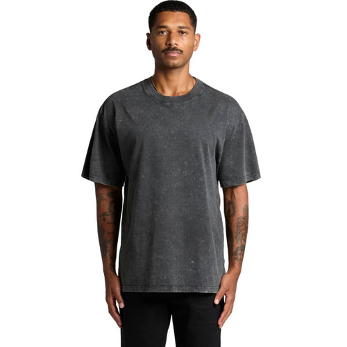 A man wearing a stone wash heavy tee in a dark grey shade. The shirt features a logo on it.