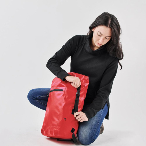 Woman adjusting red waterproof backpack for outdoor adventure.