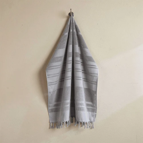 A flat terry towel in shades of grey, hanging neatly with fringed edges. It features a logo on the fabric.