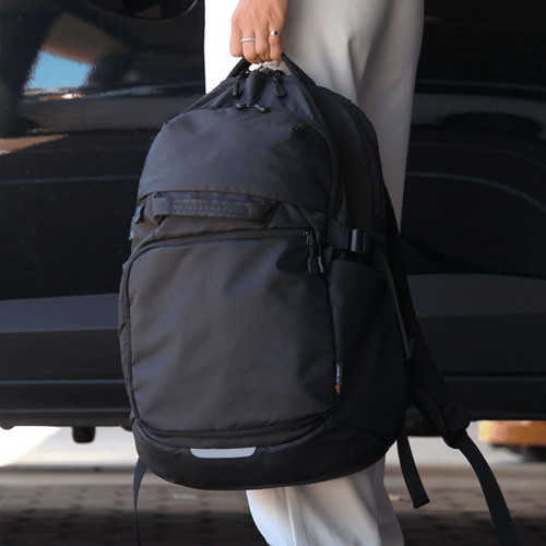 A black backpack with multiple compartments and straps, held by a person near a vehicle.