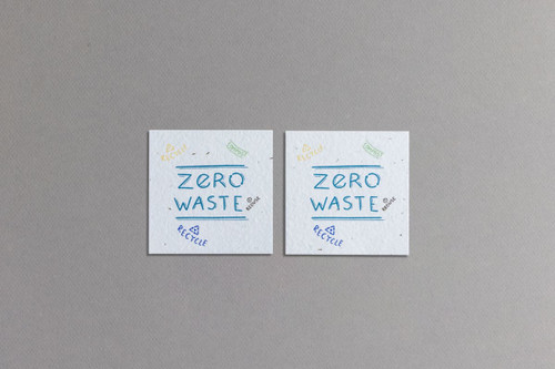 Two square pieces of textured seed paper in light grey with blue and yellow illustrations promoting zero waste.