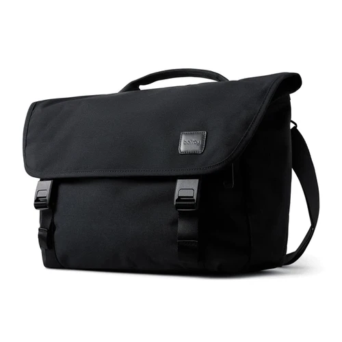 A black messenger bag featuring a flap closure, buckles, and a carrying handle, with a logo on the front.