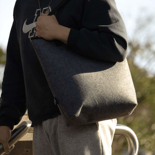 A grey recycled felt tote bag is being held by a person wearing a black hoodie and grey pants. A grey recycled felt tote bag is being held by a person wearing a black hoodie and grey pants.