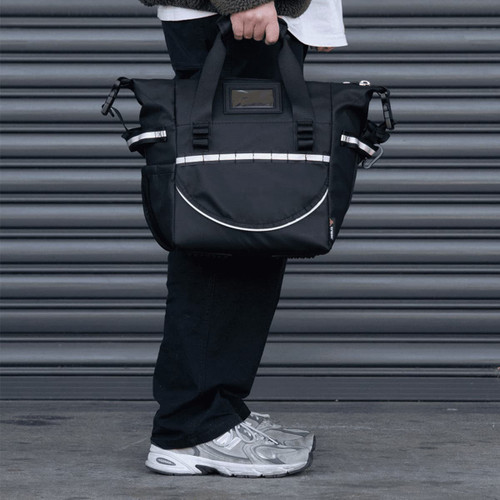 A cooler bag in black with strap and handles, featuring a logo, held by a person near a grey backdrop. A cooler bag in black with strap and handles, featuring a logo, held by a person near a grey backdrop.